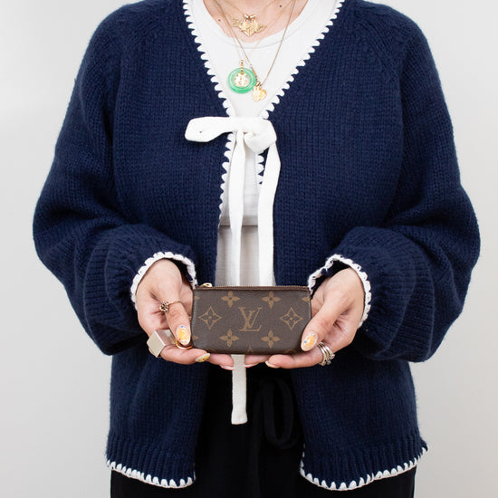 Person wearing a navy blue cardigan with white trim holding a Louis Vuitton wallet against a plain background