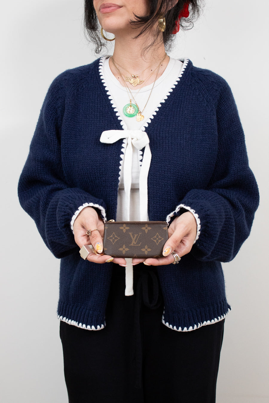 Person wearing a navy blue cardigan with white trim holding a Louis Vuitton wallet against a plain background