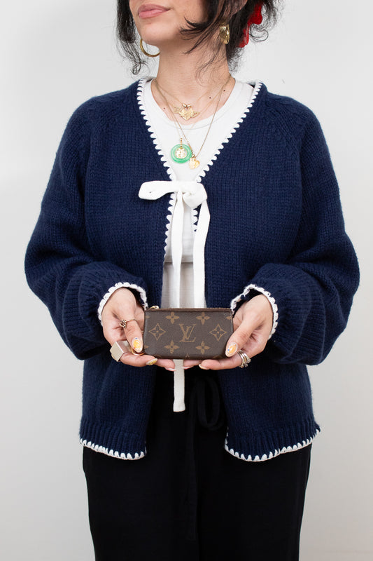 Person wearing a navy blue cardigan with white trim holding a Louis Vuitton wallet against a plain background