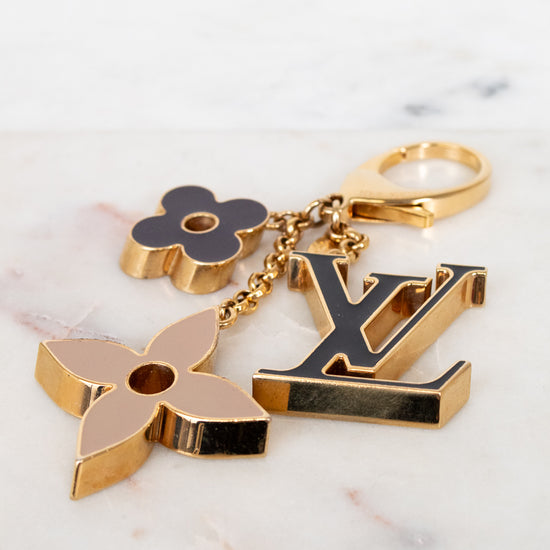 Gold keychain with floral and 'LV' logo designs on a marble surface