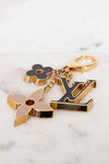Gold keychain with floral and 'LV' logo designs on a marble surface