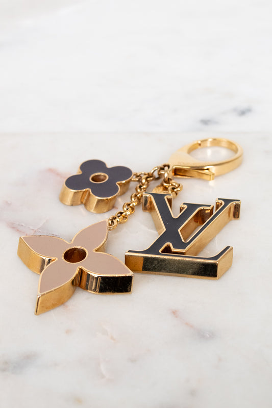 Gold keychain with floral and 'LV' logo designs on a marble surface