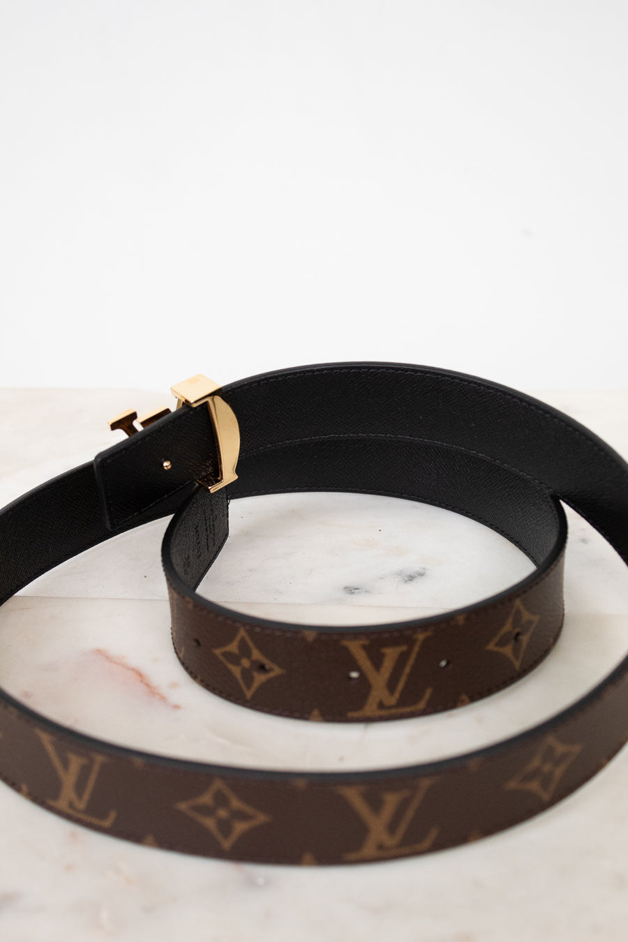 Black and brown Louis Vuitton belt showing black interior side on a marble surface