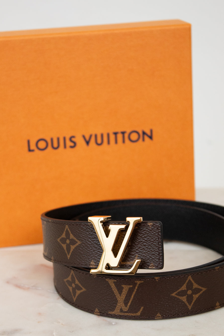 Louis Vuitton belt with monogram pattern and gold buckle with orange box background