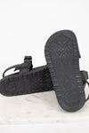A pair of black leather sandals shown from the sole side, resting on a white marble surface against a white background.