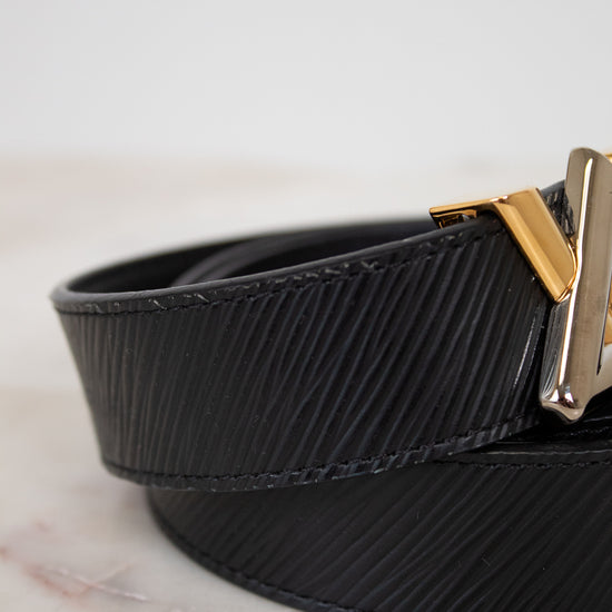 Black belt with a gold and silver buckle on a light marble background