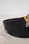 Black belt with a gold and silver buckle on a light marble background