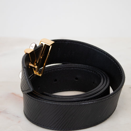Black belt with a gold buckle on a light gray background