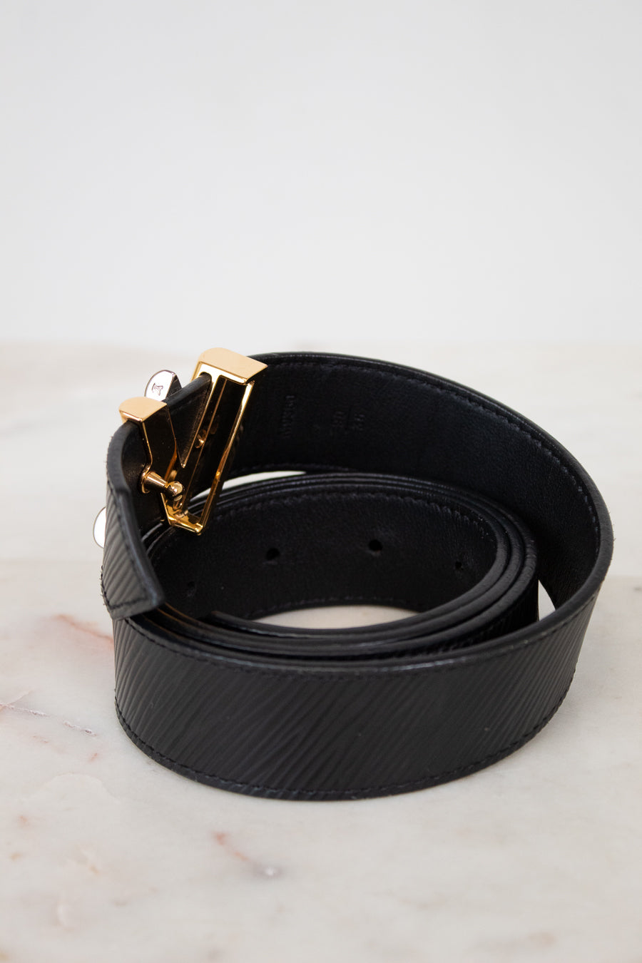 Black belt with a gold buckle on a light gray background