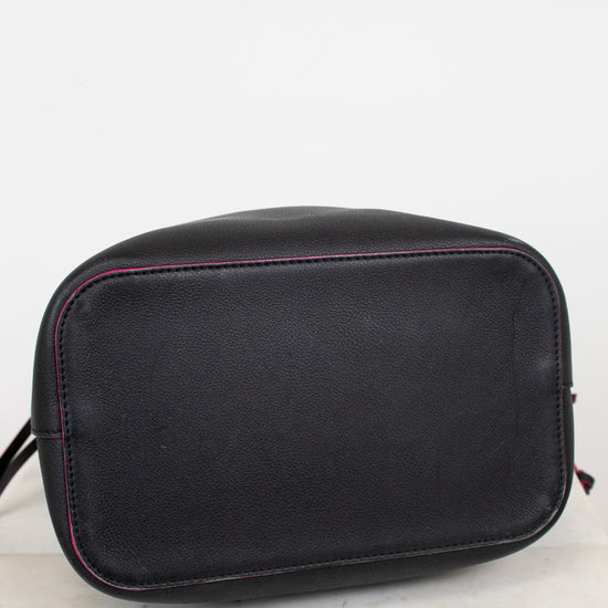 Bottom view of black leather handbag with rounded shape bottom and contrasting pink stitching, resting on a light marble surface against a white background.