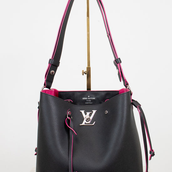 A black leather Louis Vuitton bucket bag with vibrant pink lining and trim, featuring a silver-tone LV logo on the front and a hanging leather tag, displayed on a stand against a white background.