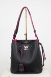 A black leather Louis Vuitton bucket bag with vibrant pink lining and trim, featuring a silver-tone LV logo on the front and a hanging leather tag, displayed on a stand against a white background.