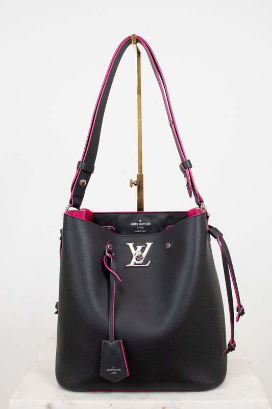 A black leather Louis Vuitton bucket bag with vibrant pink lining and trim, featuring a silver-tone LV logo on the front and a hanging leather tag, displayed on a stand against a white background.