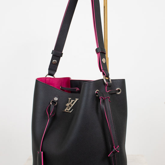 A black leather Louis Vuitton shoulder bag with a bright pink interior and pink contrast edges and lining, featuring a gold-tone metal stand on the strap and a silver-tone LV logo on the front.