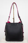 A black leather bucket tote bag with a vibrant pink interior lining and matching shoulder straps, displayed on a stand against a white background.