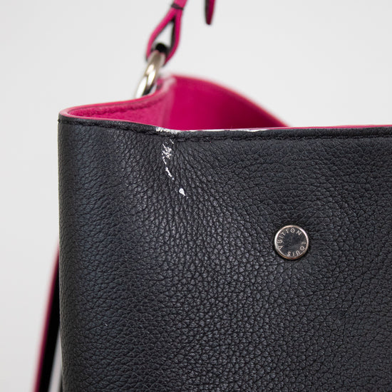 Close-up of a white mark on edge of black pebbled leather bucket bag with a bright pink interior lining and a matching pink strap, featuring a silver-tone metal rivet.