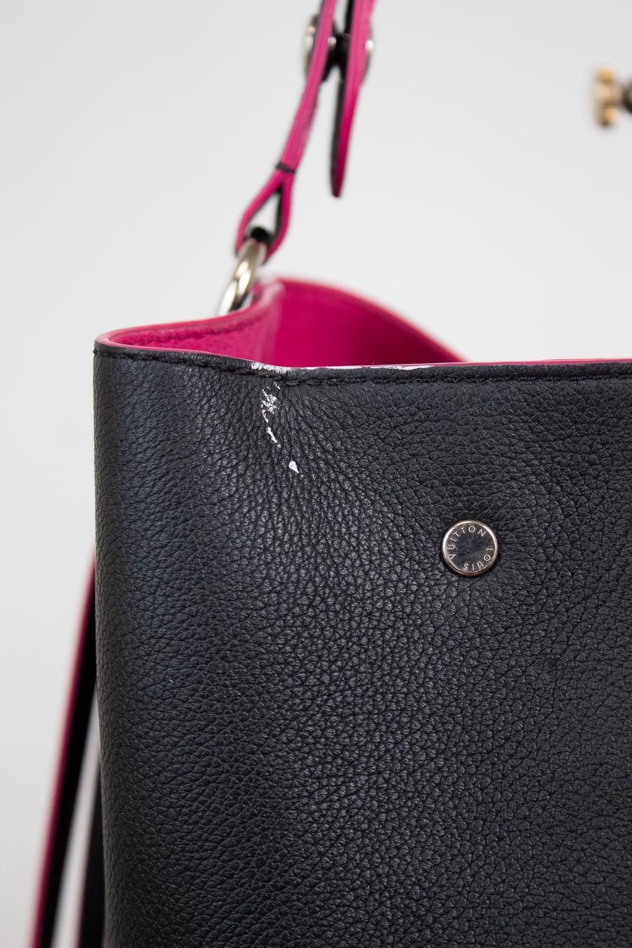 Close-up of a white mark on edge of black pebbled leather bucket bag with a bright pink interior lining and a matching pink strap, featuring a silver-tone metal rivet.
