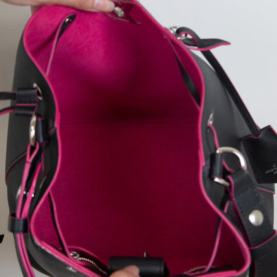 A close-up of a black leather handbag with a bright pink interior lining, held open by two hands against a plain light background.