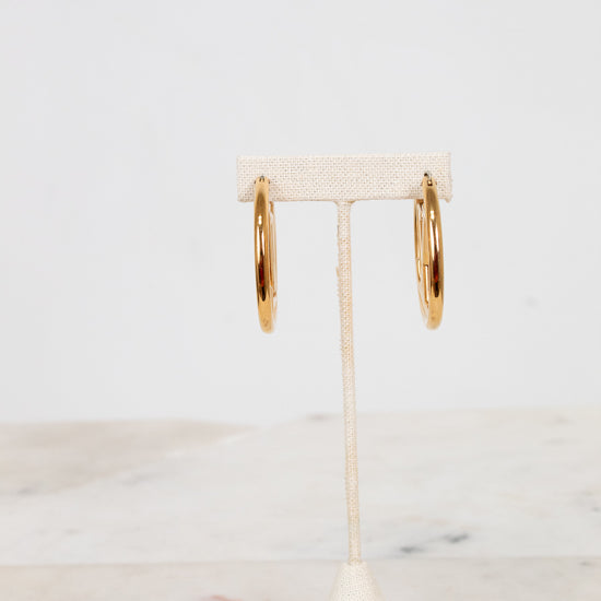 Gold hoop earrings on a white stand with a marble surface background