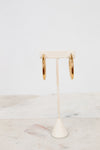 Gold hoop earrings on a white stand with a marble surface background