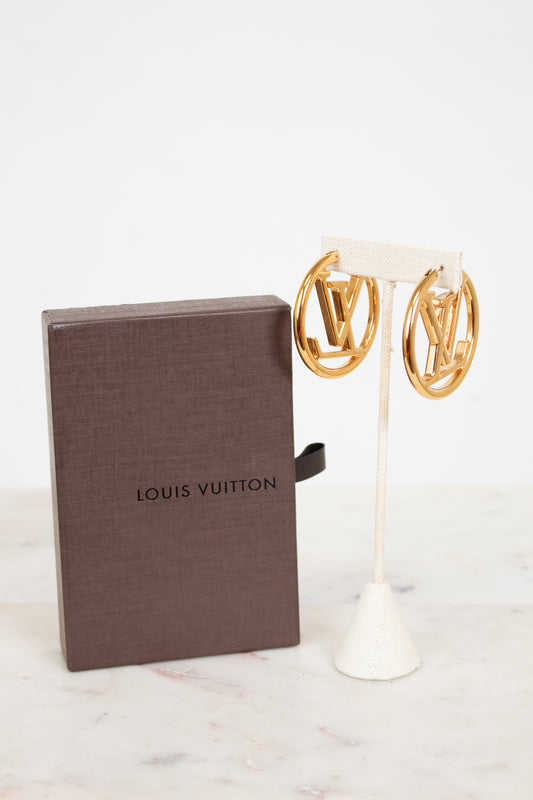 Gold earrings on a stand next to a Louis Vuitton box on a white background
