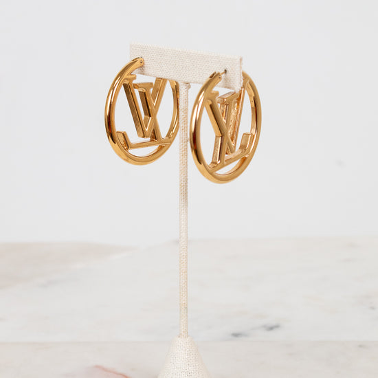 Gold hoop earrings on a white stand with a light background