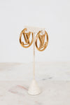 Gold hoop earrings on a white stand with a light background