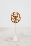 Gold circular hoop earrings with a logo on a white stand against a light background
