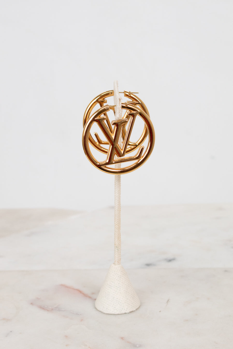 Gold circular hoop earrings with a logo on a white stand against a light background