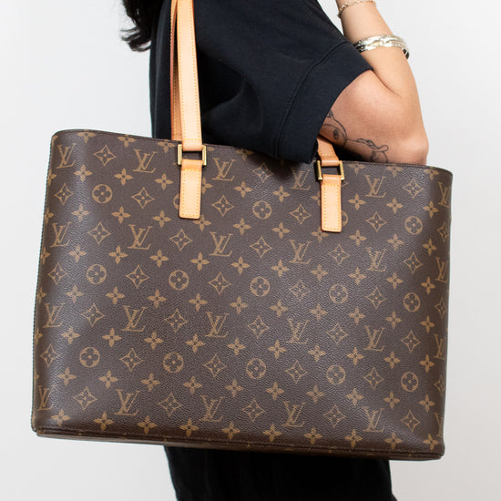 Person in black clothing holding a monogram patterned brown tote on a white background