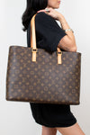 Person in black clothing holding a monogram patterned brown tote on a white background