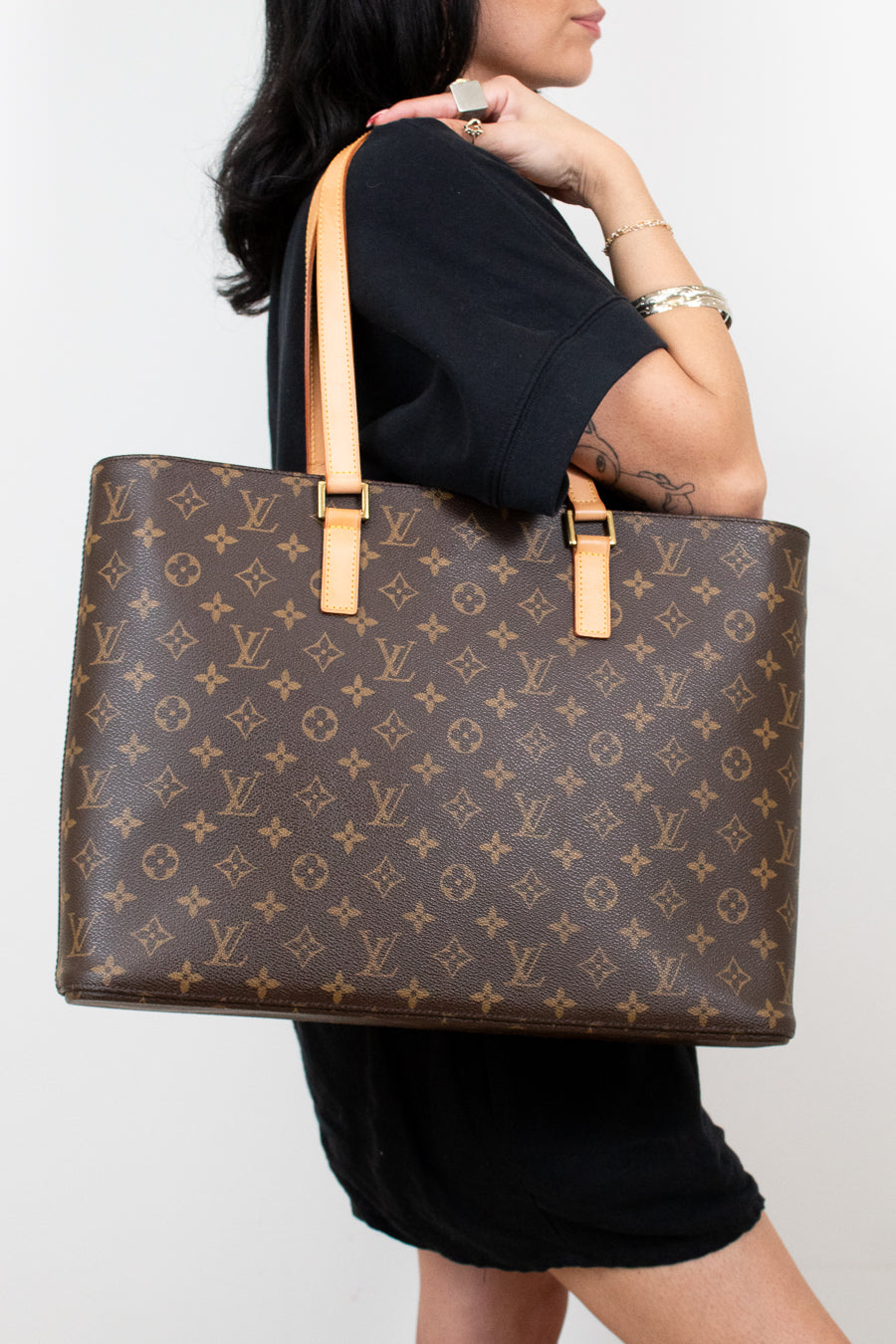 Person in black clothing holding a monogram patterned brown tote on a white background