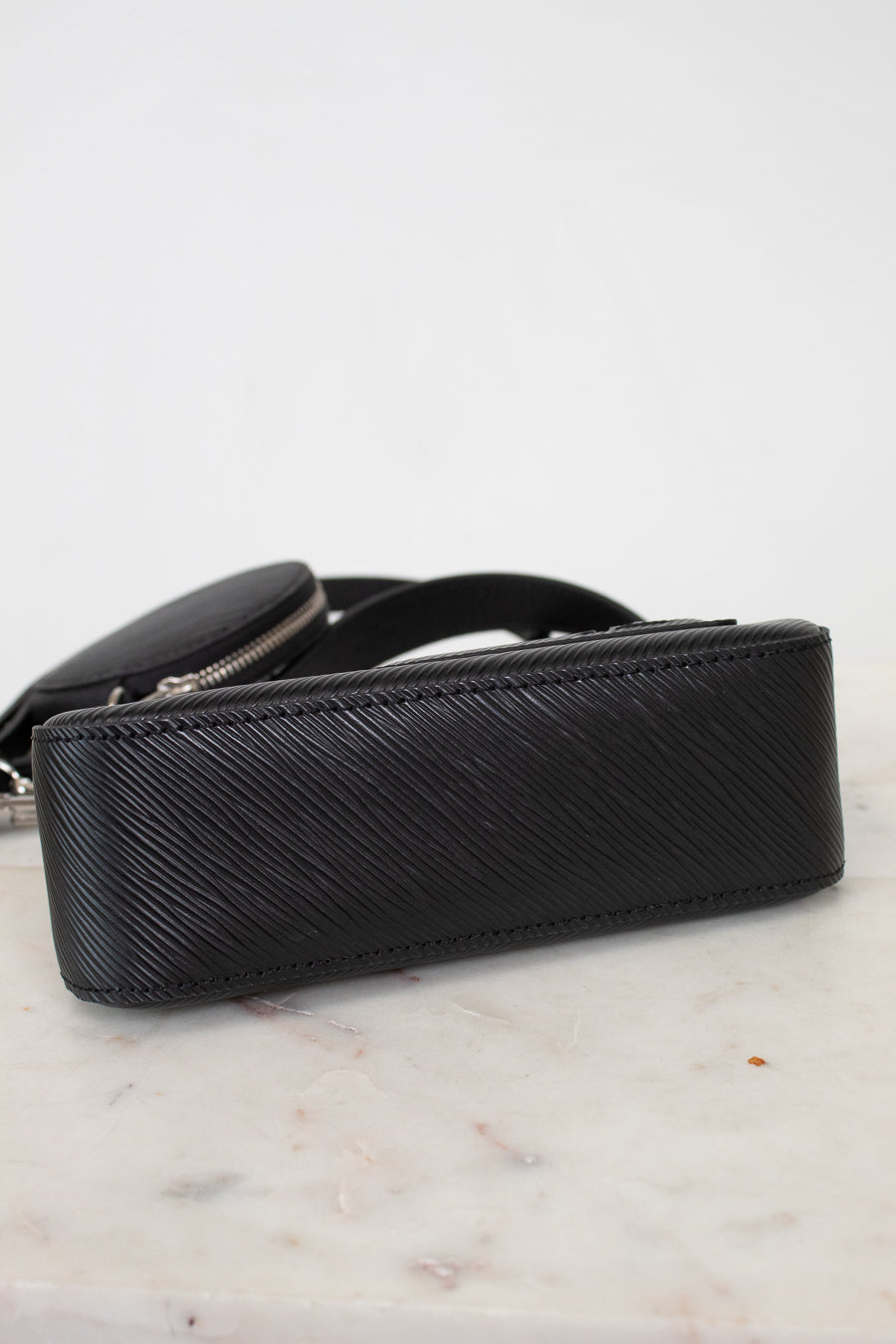 Bottom of black textured handbag on a marble surface with a light gray background