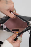 Person opening a black handbag with silver zippers on a light gray background