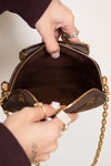 Person holding a brown handbag with gold chain strap against a neutral background