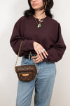 Person wearing a maroon sweater and blue jeans with a brown handbag against a plain background