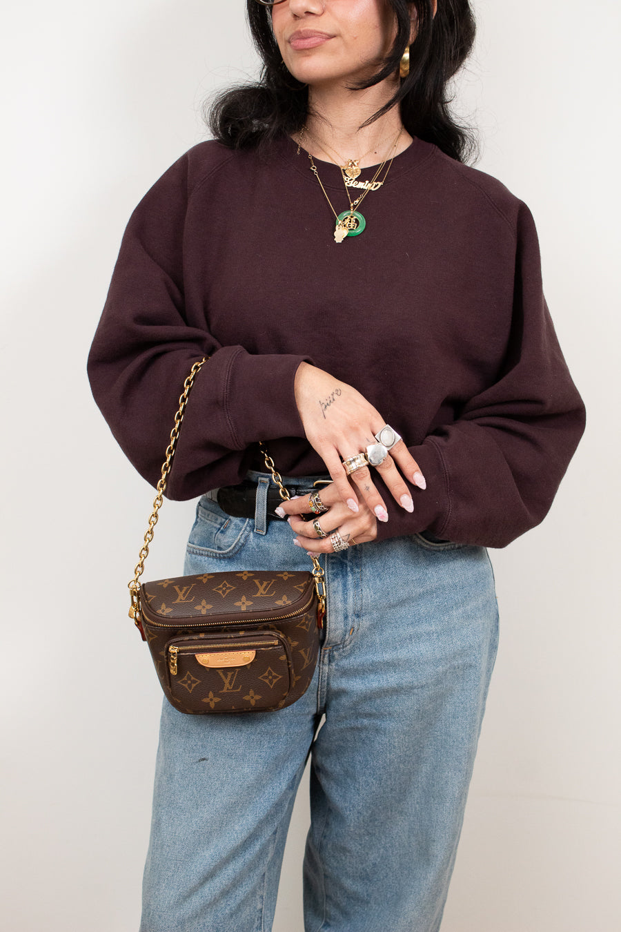 Person wearing a maroon sweater and blue jeans with a brown handbag against a plain background