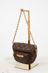 Louis Vuitton monogram handbag with gold chain on a stand against a white background