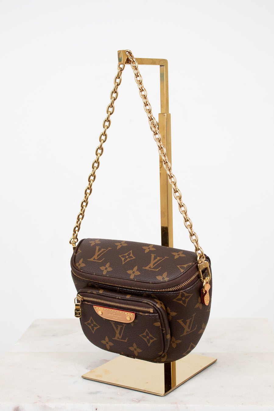 Louis Vuitton monogram handbag with gold chain on a stand against a white background