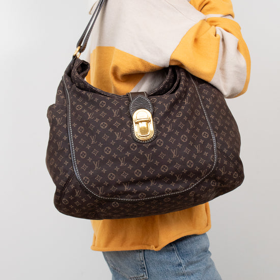 Person wearing a yellow and white sweater with a brown patterned handbag on a plain background