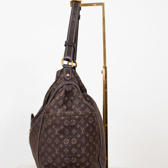 Brown monogram handbag on a gold stand against a white background