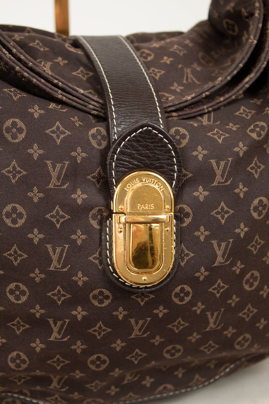Close-up of a brown Louis Vuitton handbag with gold fastener on a light gray background
