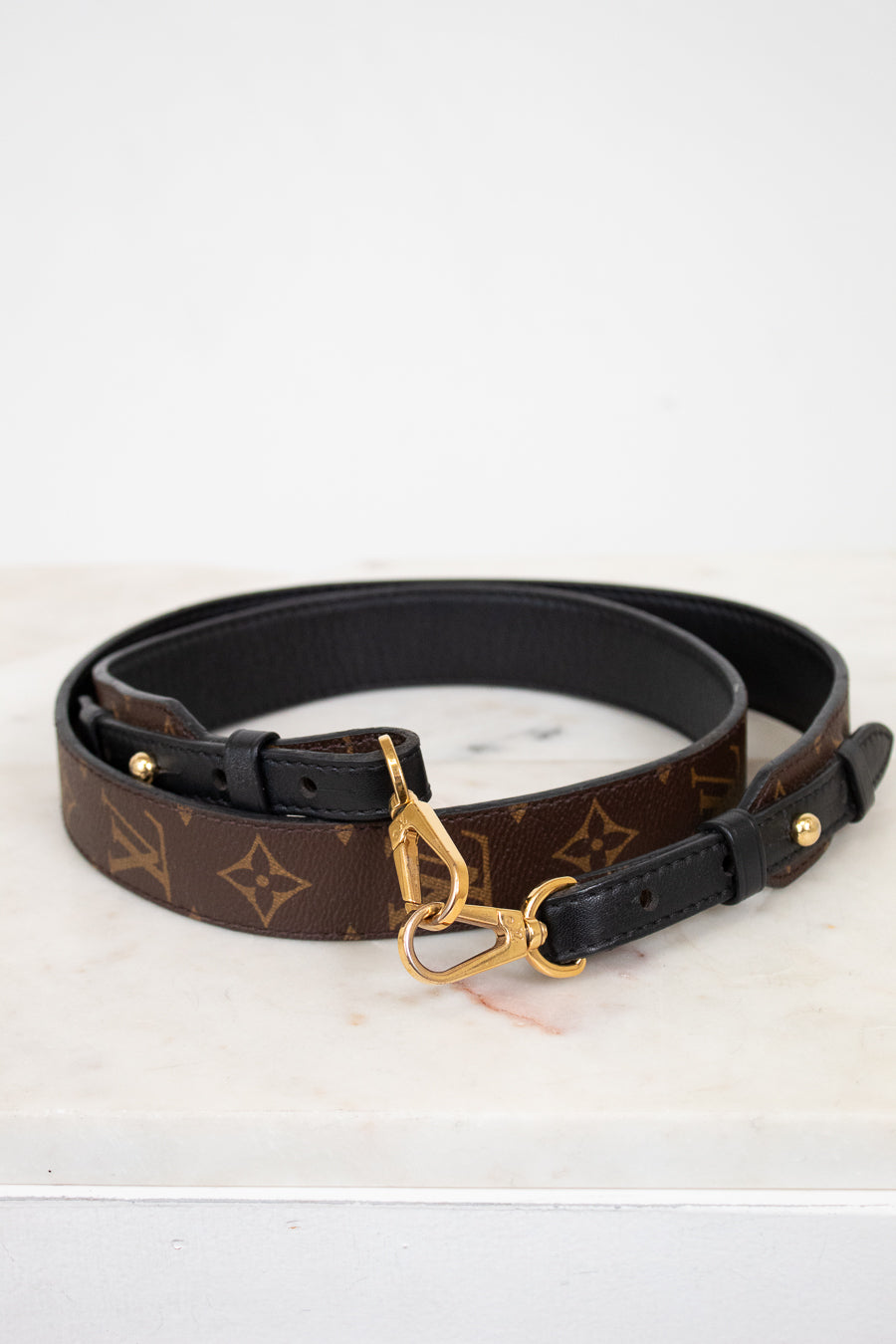 Designer belt with monogram pattern and gold buckle on a white background