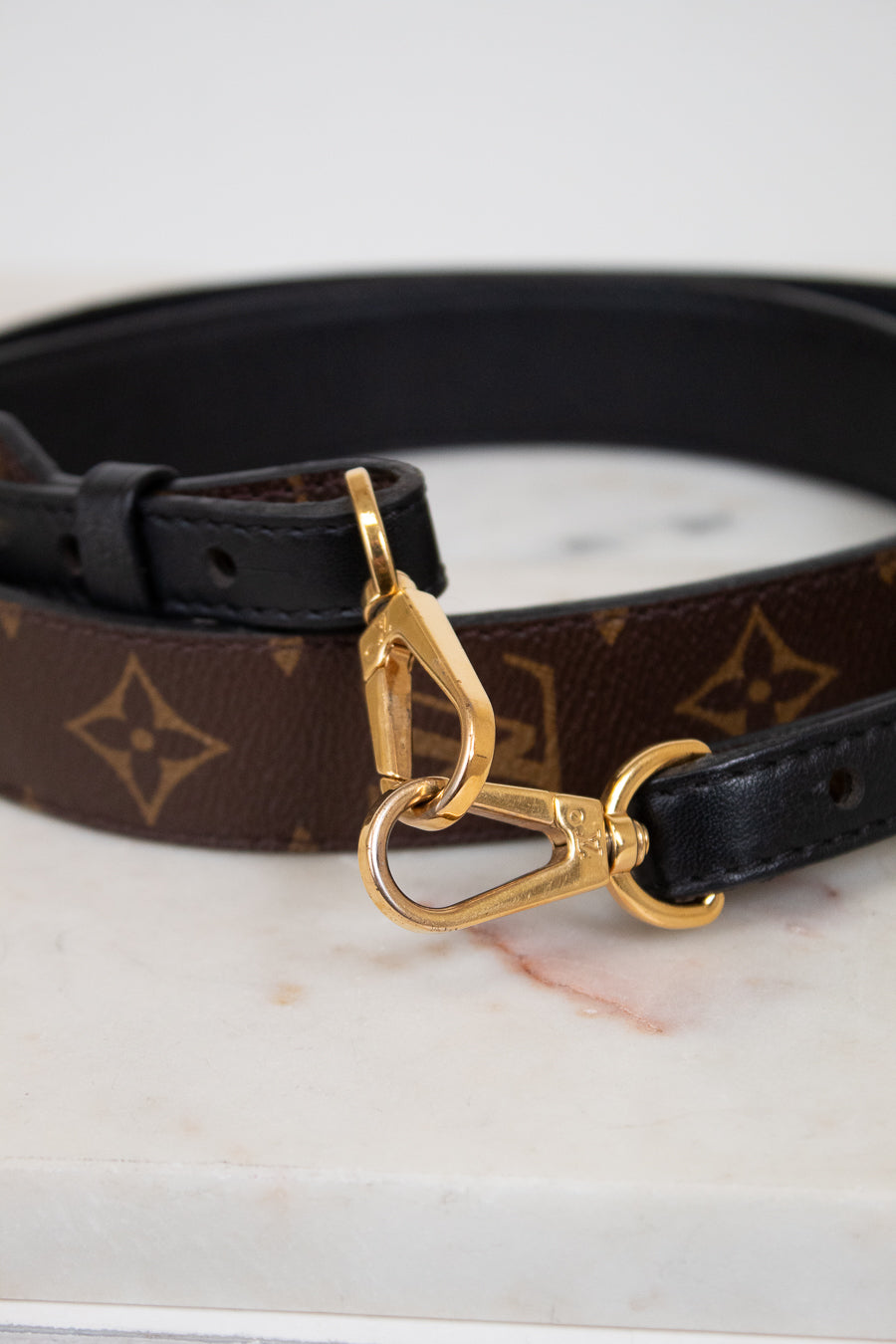 Handbag strap with gold clasp on a marble surface
