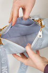 Light blue handbag with gold zipper being held open by a hand on a light gray background