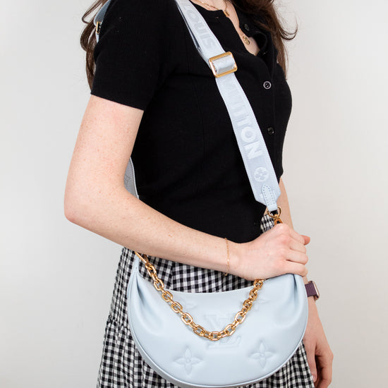 Woman wearing a light blue handbag with a gold chain strap against a plain background