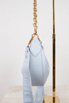 Light blue handbag with gold chain strap on a white background