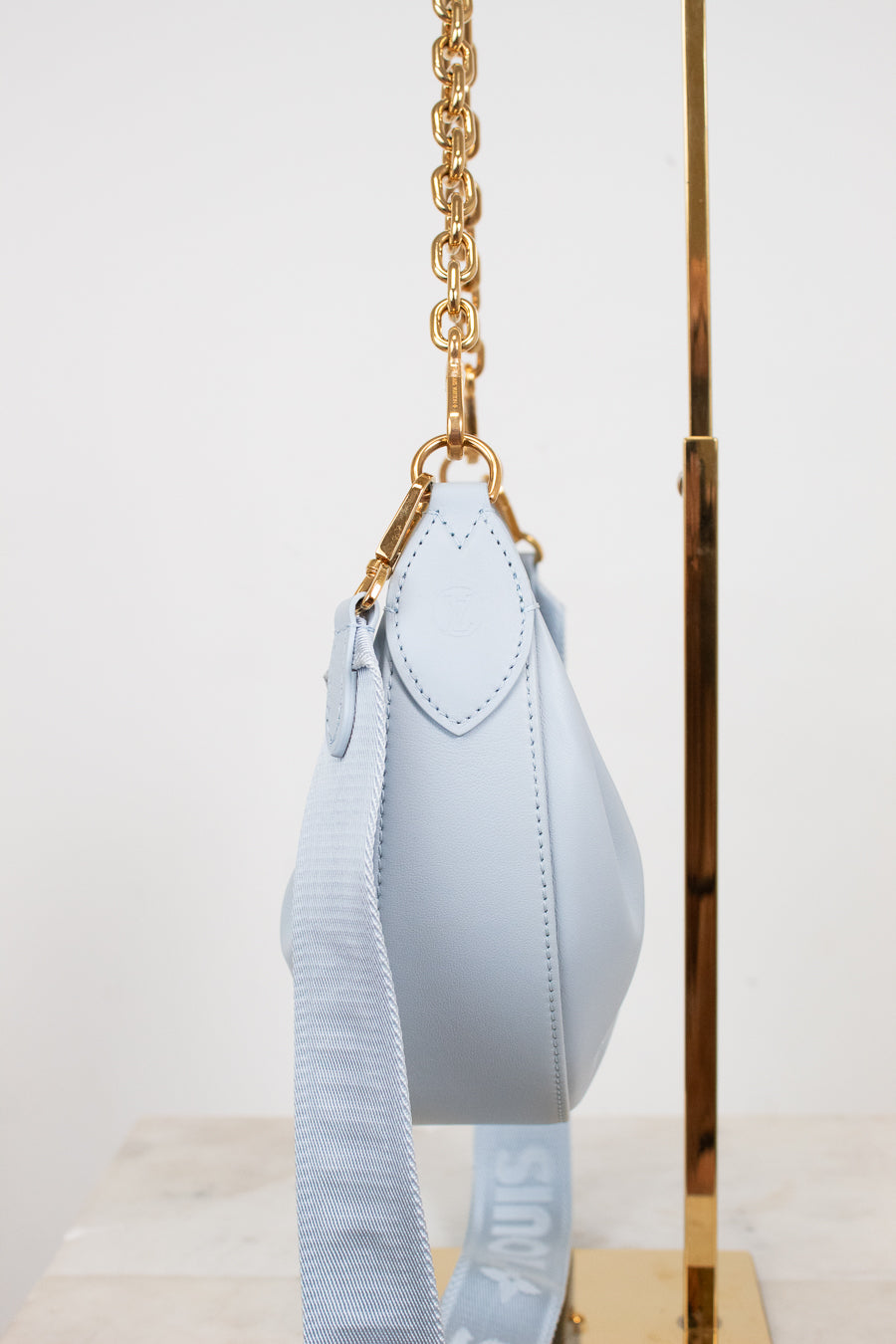 Light blue handbag with gold chain strap on a white background