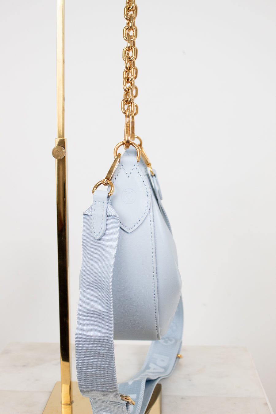 Light blue handbag with gold chain strap on a white background