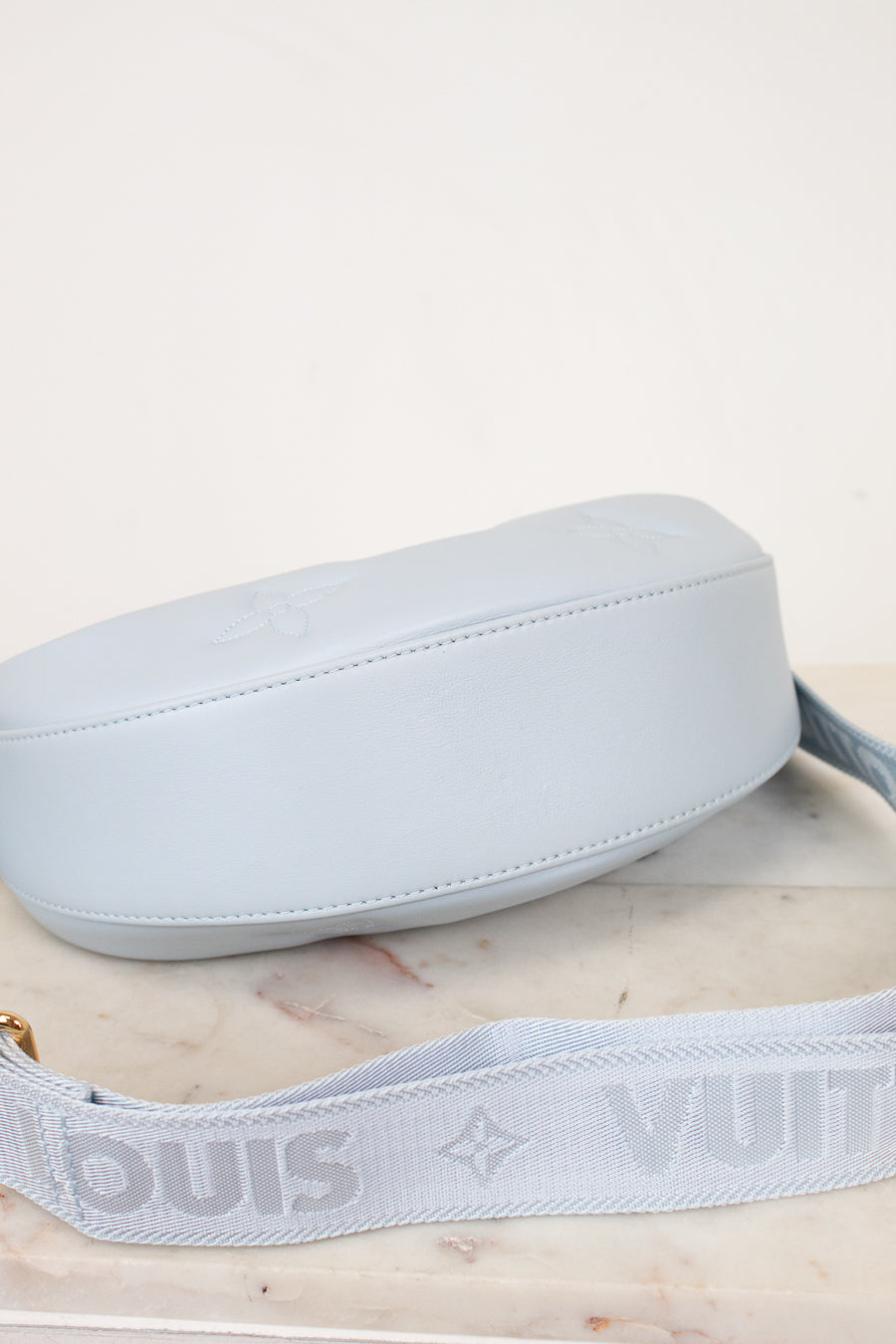Light blue bottom exterior of handbag with strap on a light marble surface